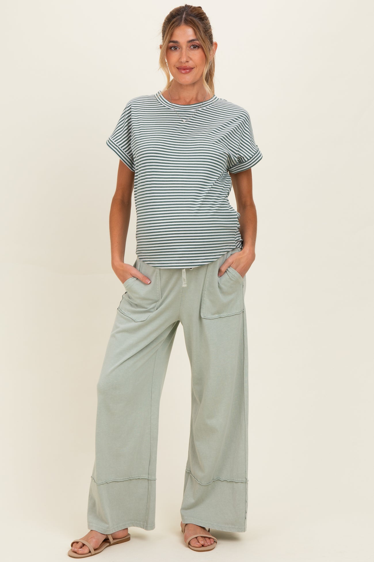 woman wearing a striped maternity top and light green wide-leg maternity pants with pockets, posing with a baby bump visible