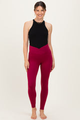 woman wearing a black sleeveless maternity top and burgundy high-waisted maternity leggings, standing barefoot