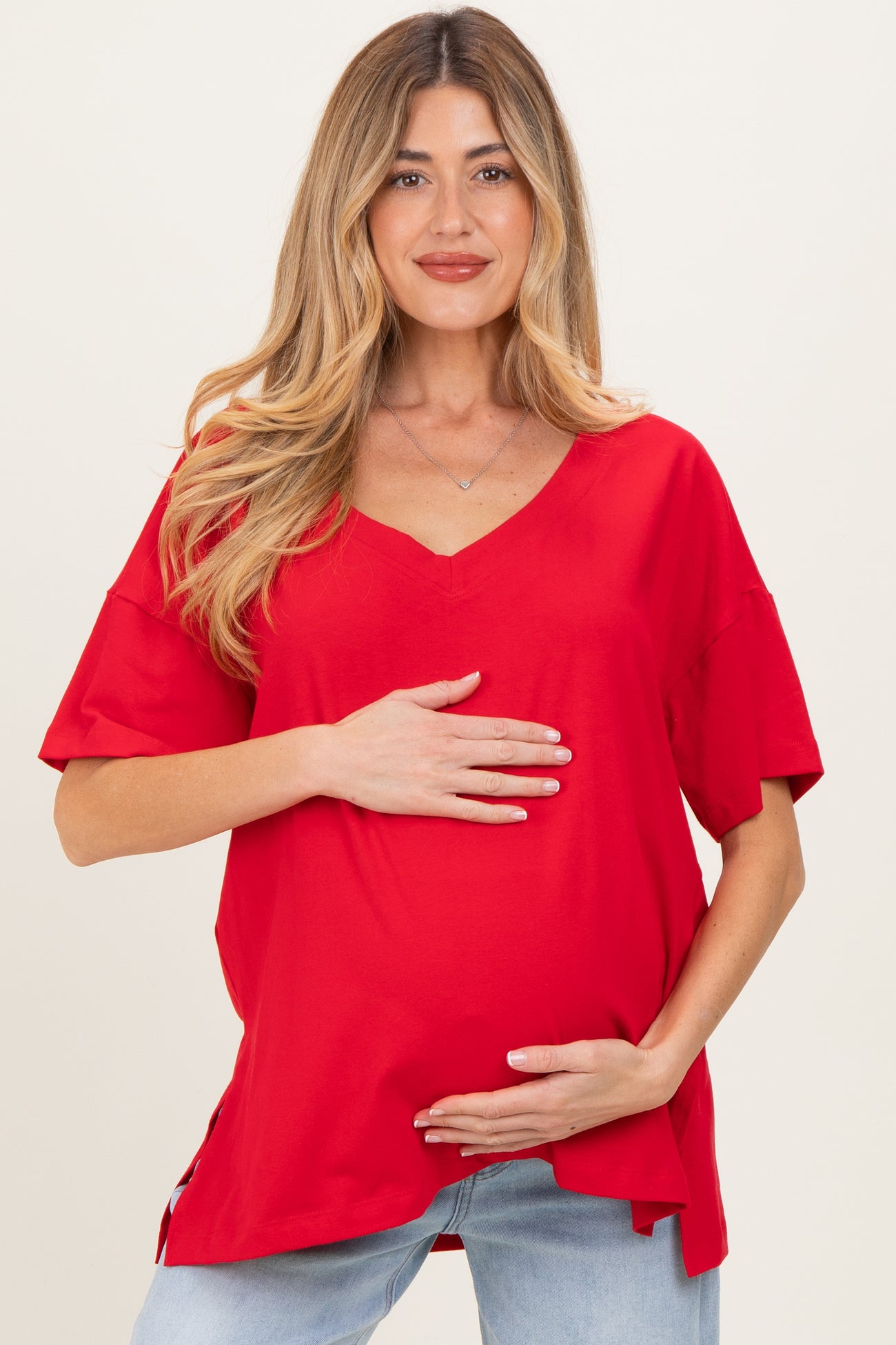 woman wearing a red short sleeve maternity top and holding her baby bump