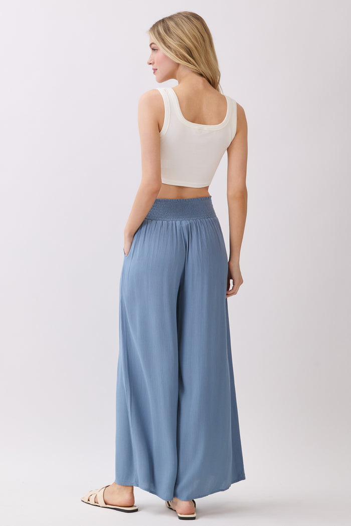 woman wearing a white cropped tank top and light blue wide-leg pants with an elastic waistband, standing with her back to the camera