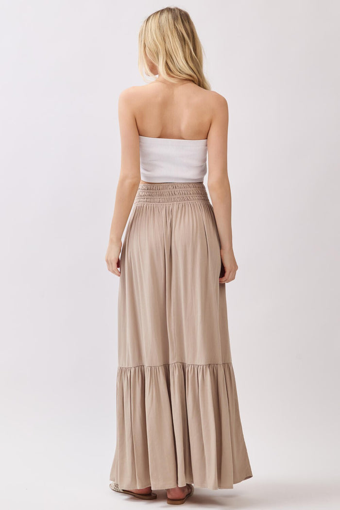 woman wearing a strapless white smocked top and a long beige tiered maxi skirt, viewed from the back
