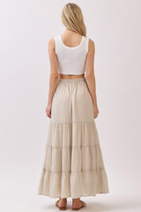 woman wearing a white cropped tank top and a long beige tiered maxi skirt, seen from the back