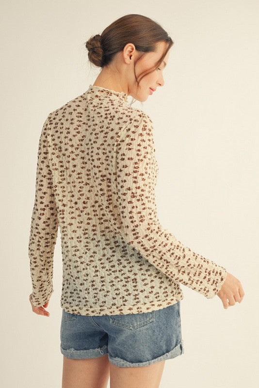 woman wearing a long sleeve cream top with a floral pattern and denim shorts, viewed from the back