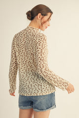 woman wearing a long sleeve cream top with a floral pattern and denim shorts, viewed from the back
