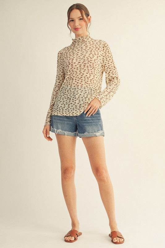 woman wearing a patterned long sleeve top with a high neckline and denim shorts, standing in a relaxed pose