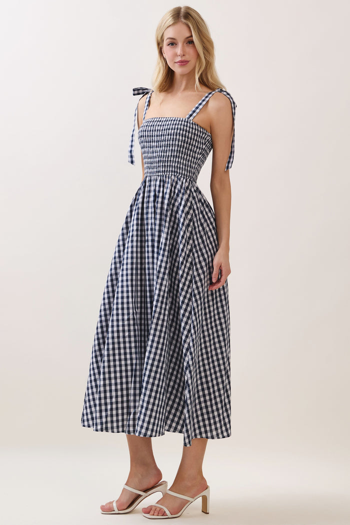 woman wearing a navy and white gingham midi dress with smocked bodice and tie shoulder straps