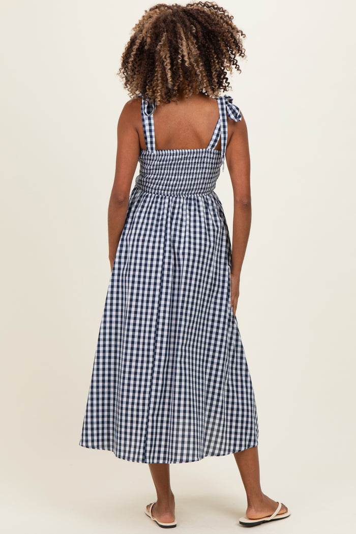 woman wearing a navy and white gingham maternity maxi dress with tie straps and a smocked back