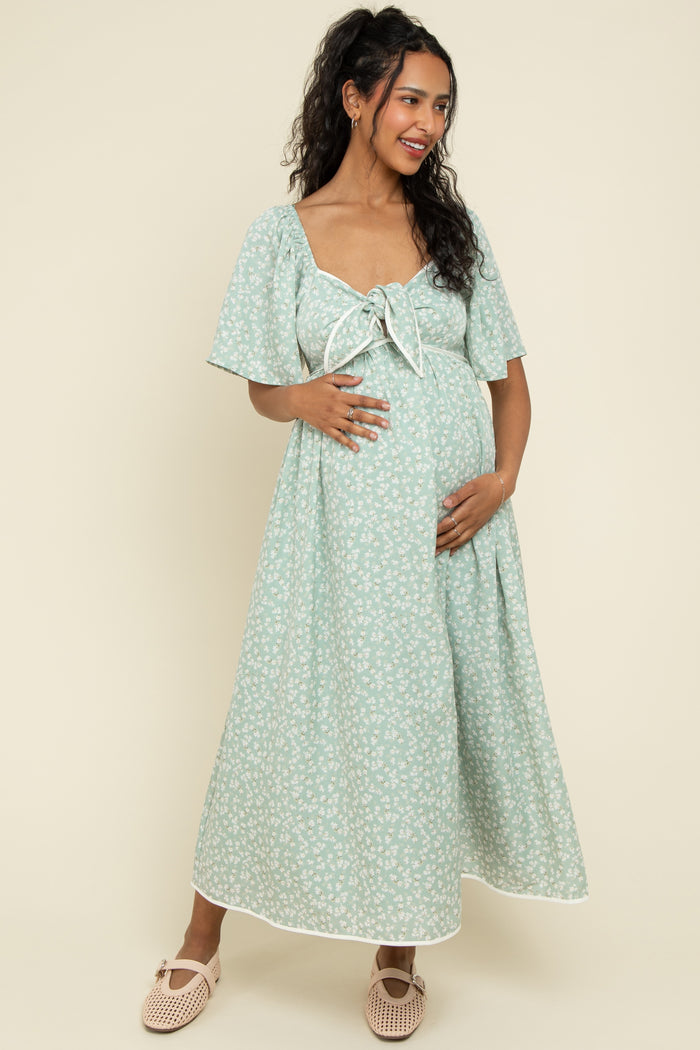 woman wearing a mint green floral maternity maxi dress with a tie front and short sleeves, holding her baby bump