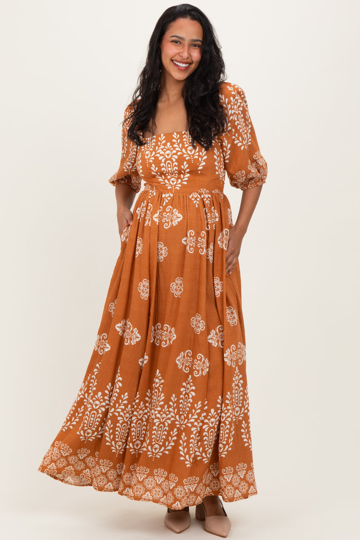 woman wearing an orange maternity maxi dress with white floral patterns and puff sleeves, showing her baby bump