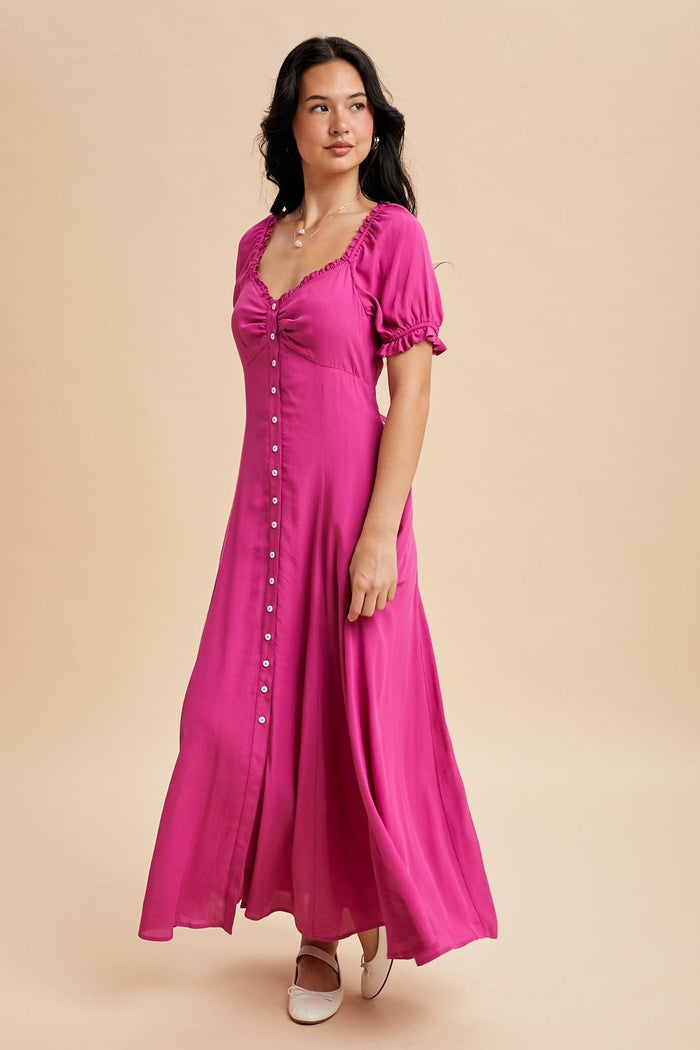 woman wearing a pink maxi dress with puff sleeves and button details, standing against a neutral background
