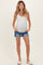 woman wearing a white ribbed tank top and distressed denim shorts, showing her baby bump