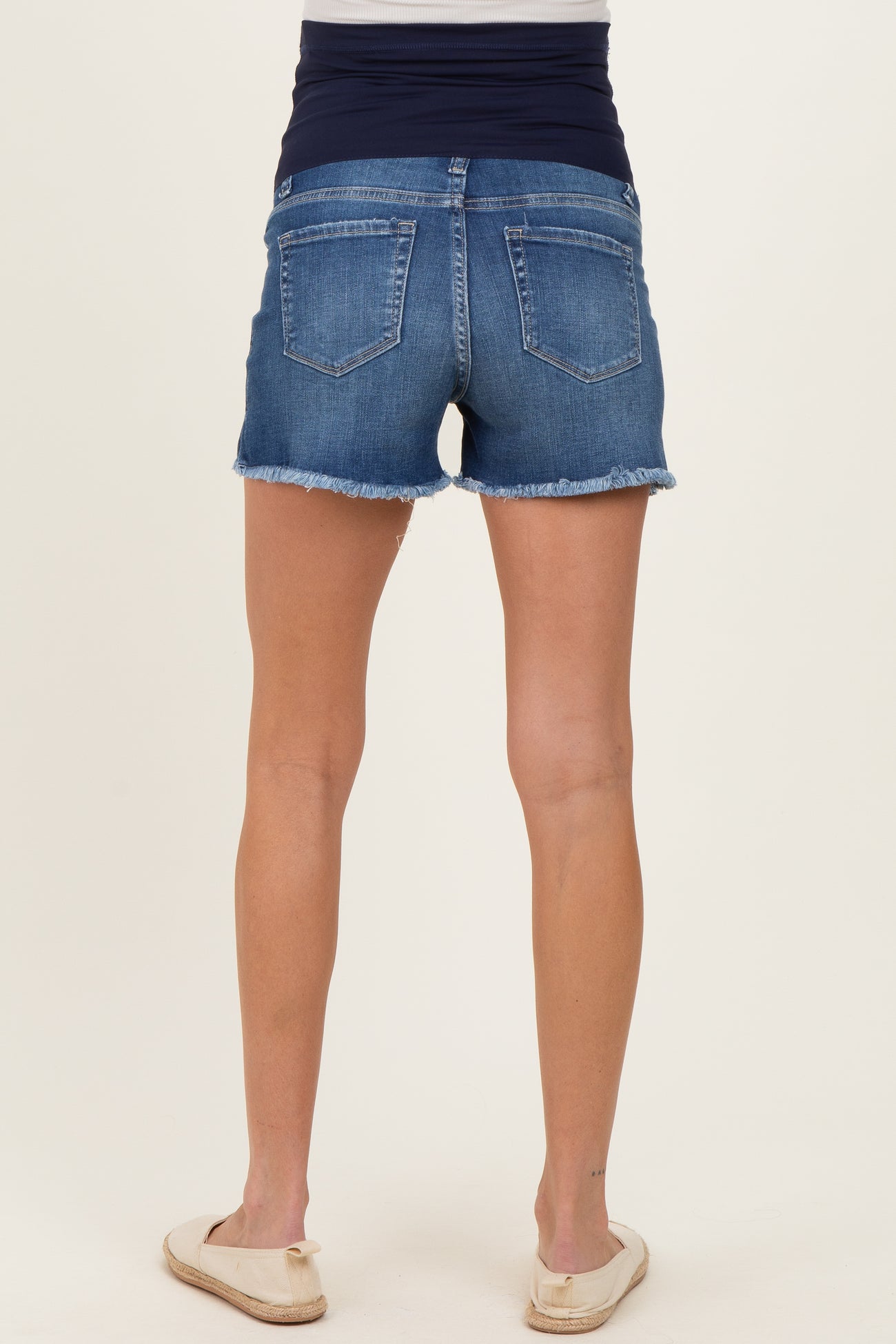 woman wearing blue maternity shorts with a frayed hem and a navy waistband, showing her back