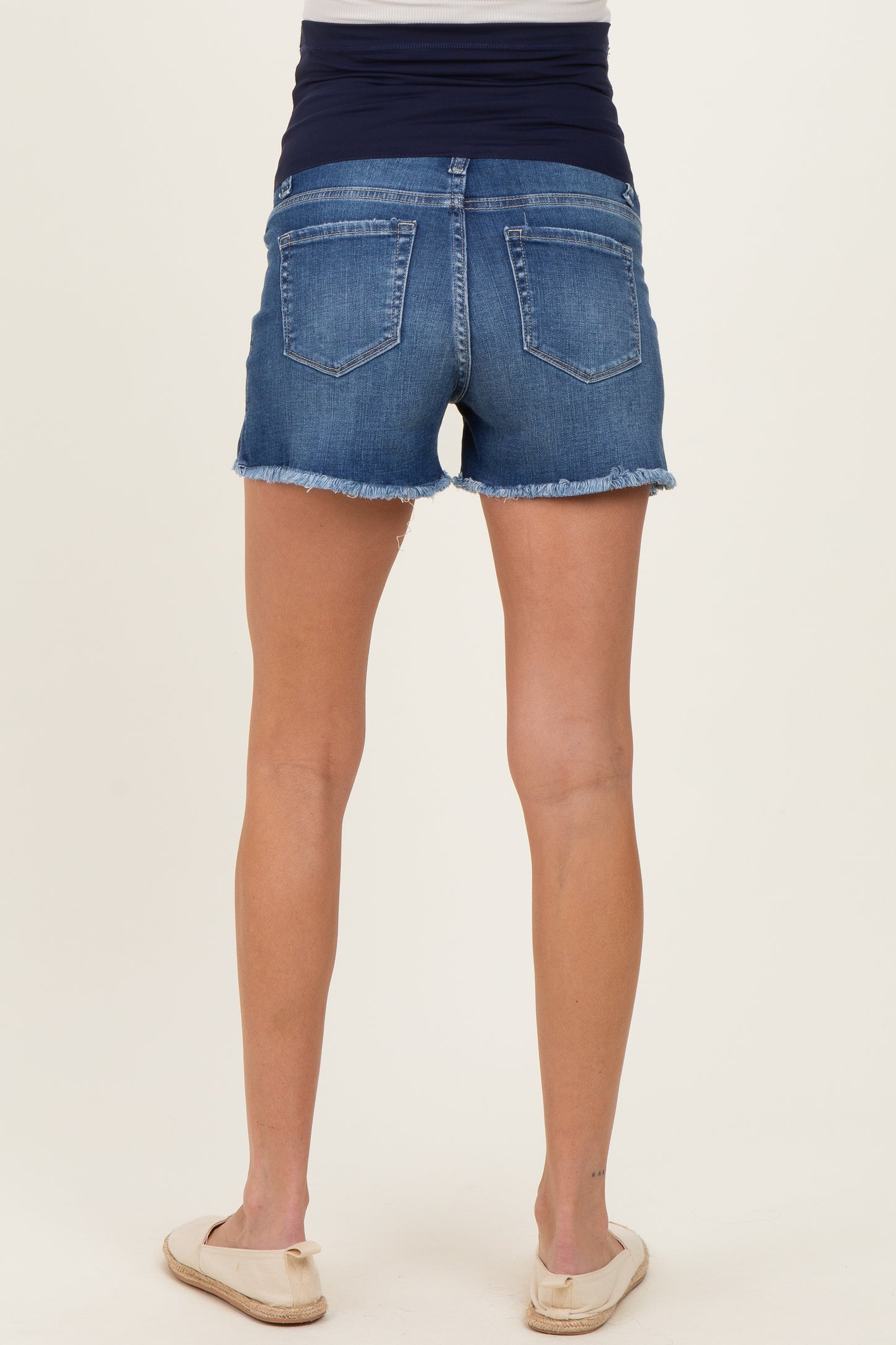 woman wearing blue maternity shorts with a frayed hem and a navy waistband, showing her back