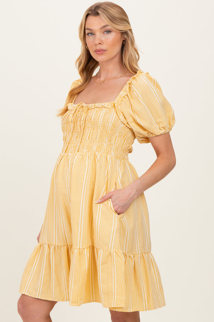 woman wearing a yellow gingham maternity dress with puff sleeves and a tiered skirt, featuring pockets
