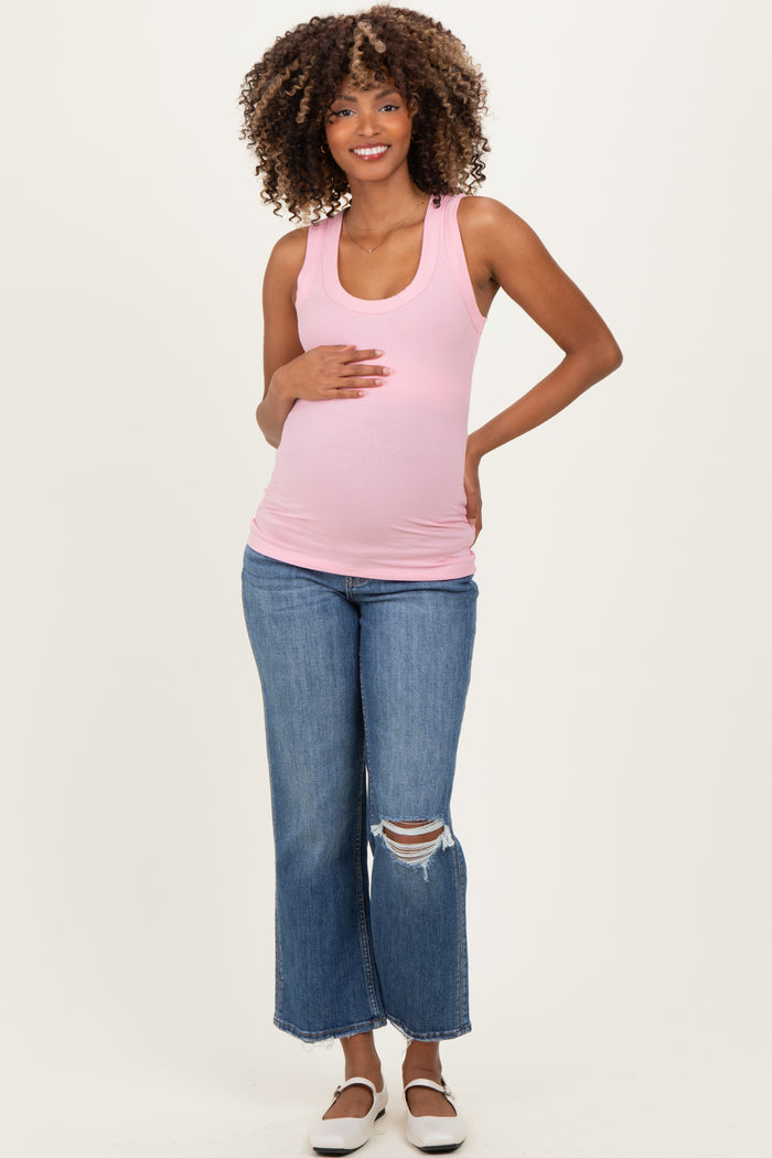 woman wearing a light pink ribbed maternity tank top and distressed flared jeans, holding her baby bump