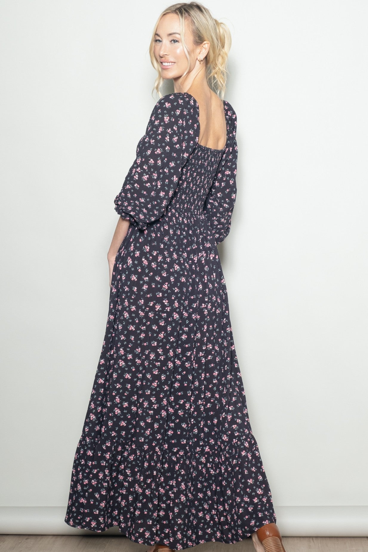 woman wearing a black floral maxi dress with puff sleeves and a smocked back, posing sideways against a light background