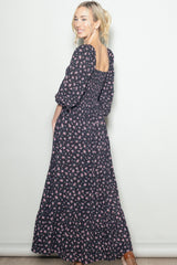 woman wearing a black floral maxi dress with puff sleeves and a smocked back, posing sideways against a light background