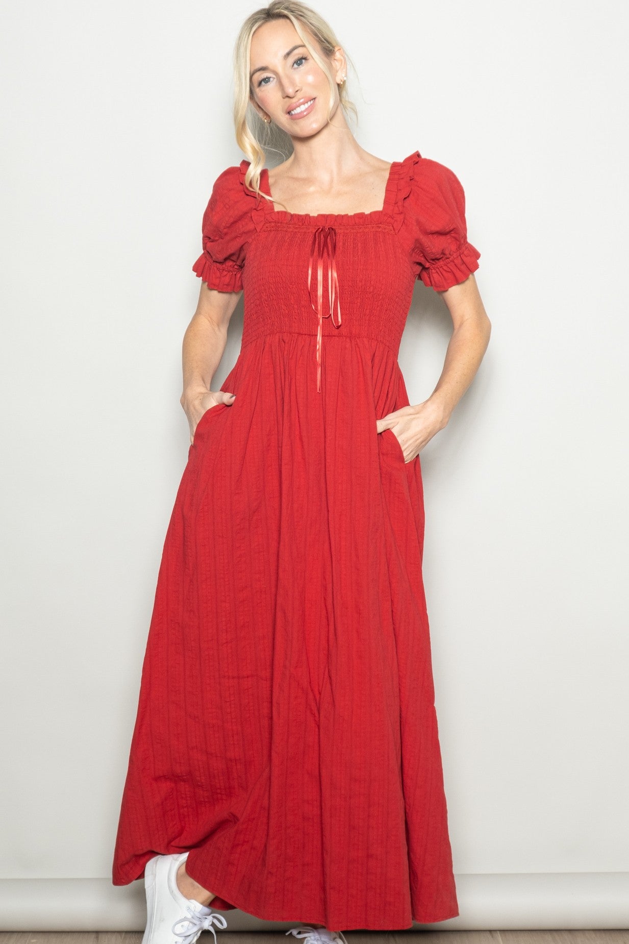 woman wearing a red maxi dress with puff sleeves and pockets, styled with white sneakers
