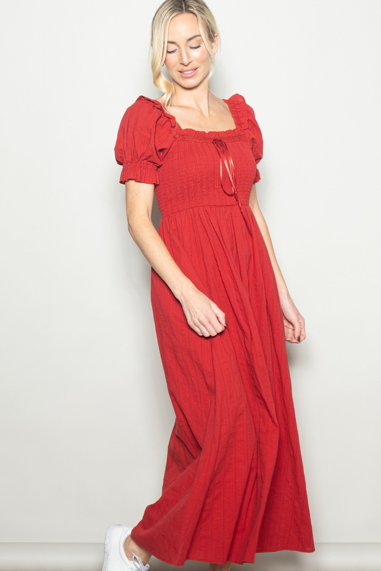 woman wearing a red long puff sleeve maxi dress with a square neckline and smocked bodice, paired with white sneakers