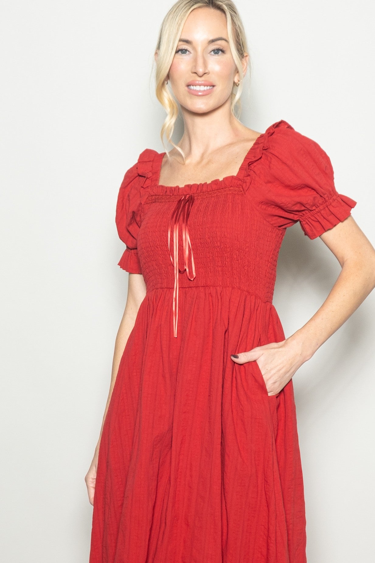 woman wearing a red smocked dress with puff sleeves and pockets, smiling at the camera