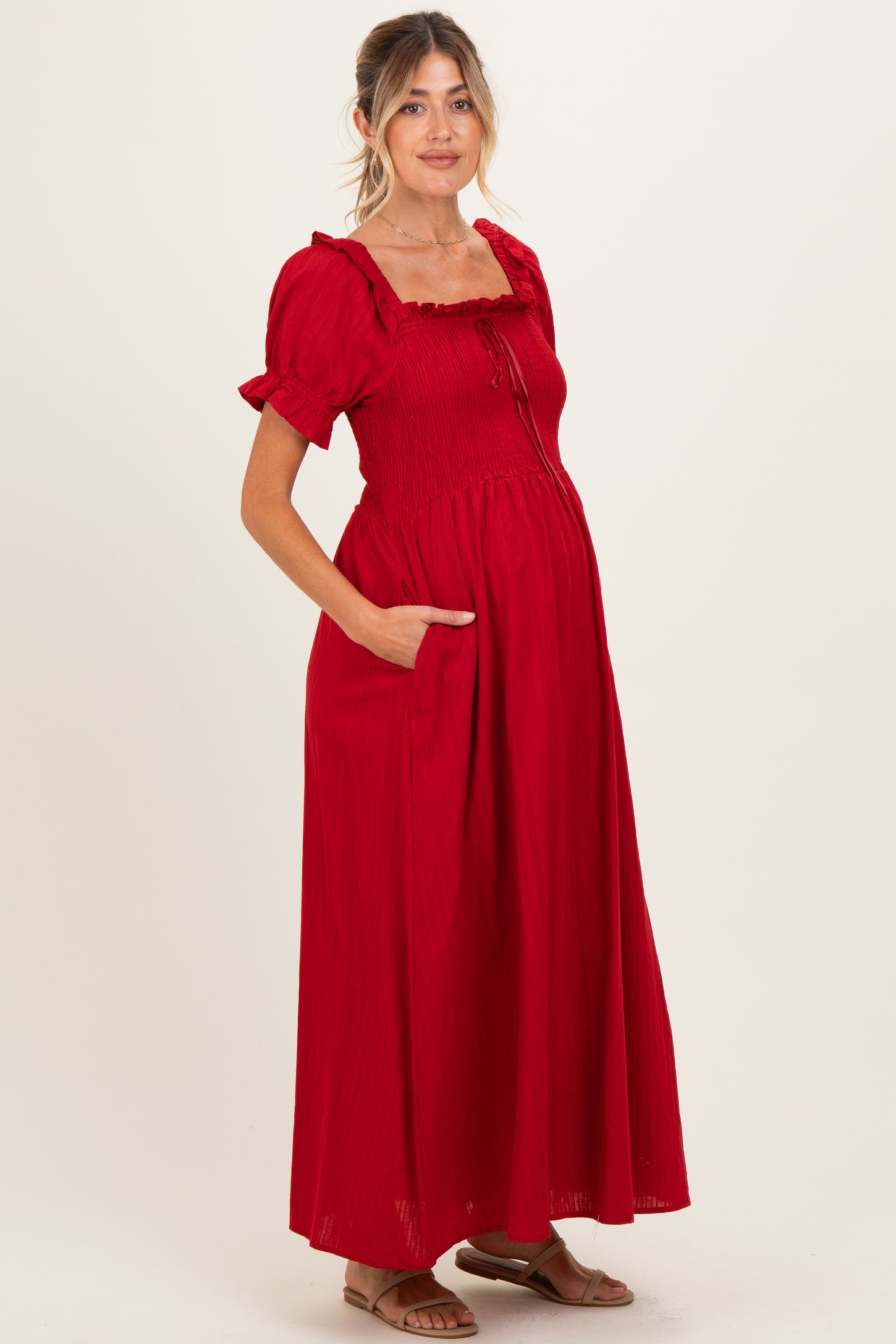 woman wearing a red maternity maxi dress with smocked bodice, short puff sleeves, and pockets