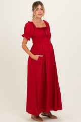 woman wearing a red maternity maxi dress with smocked bodice, short puff sleeves, and pockets