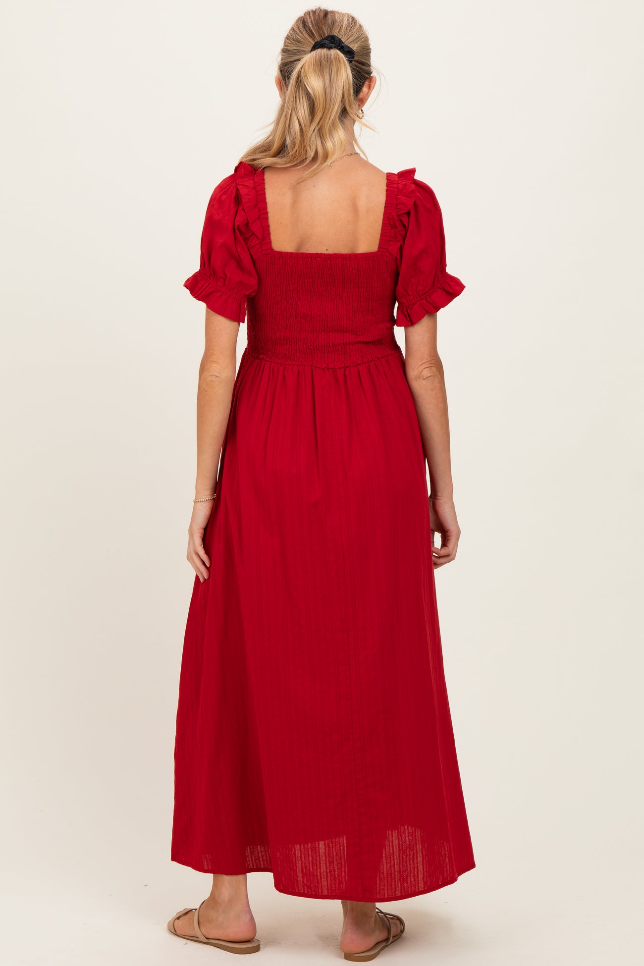 woman wearing a red maternity maxi dress with short puff sleeves and a smocked bodice, focused on the back view