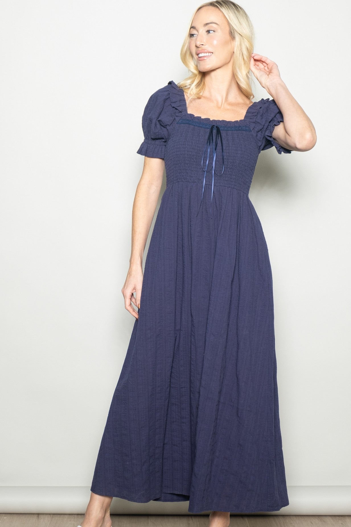 woman wearing a navy blue puff sleeve maxi dress with a square neckline and tie detail