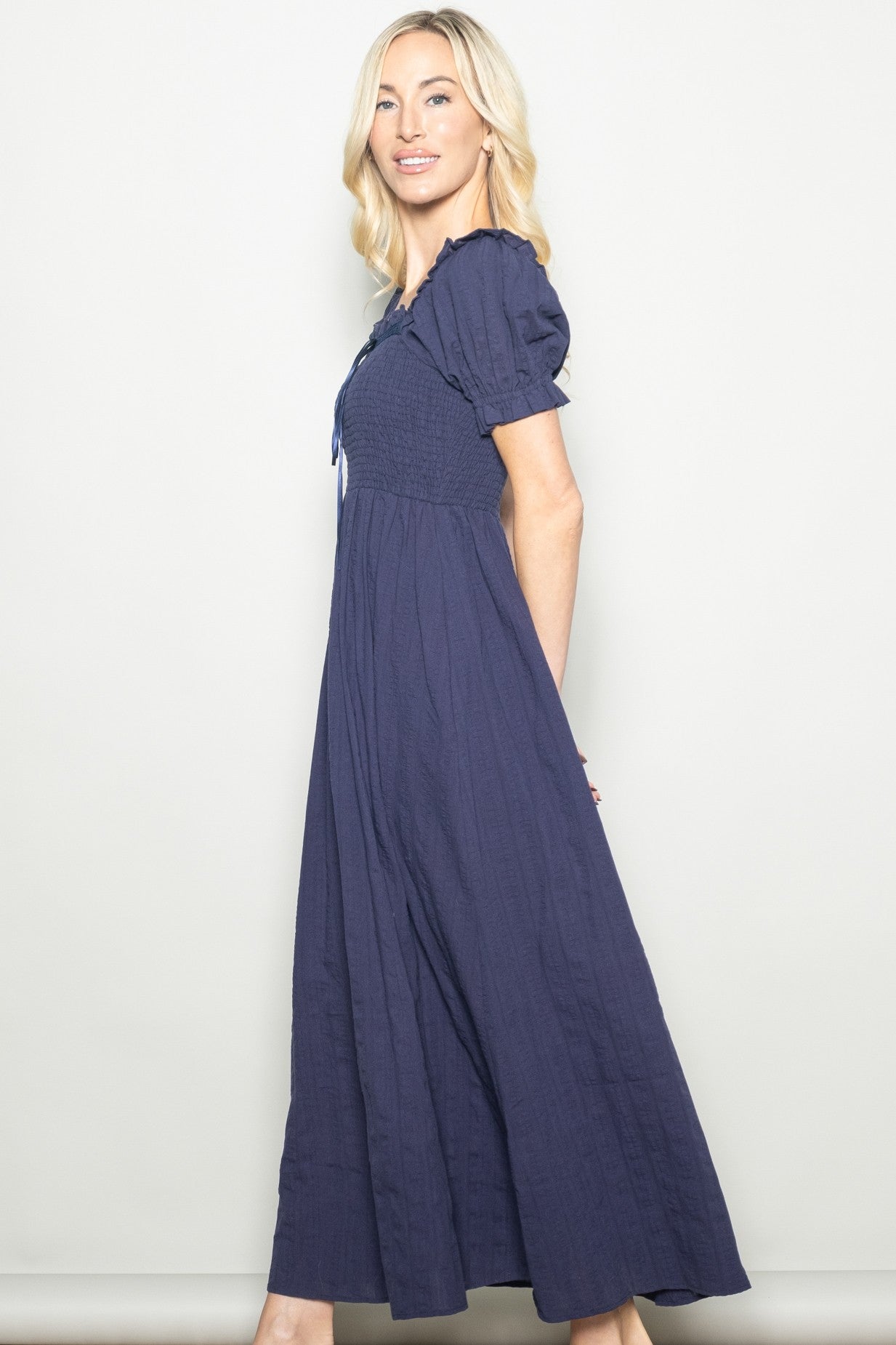 woman wearing a navy blue long maxi dress with puff sleeves and a smocked bodice, posed against a neutral background