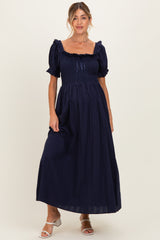 woman wearing a navy blue maternity maxi dress with puff sleeves and a smocked bodice, smiling at the camera