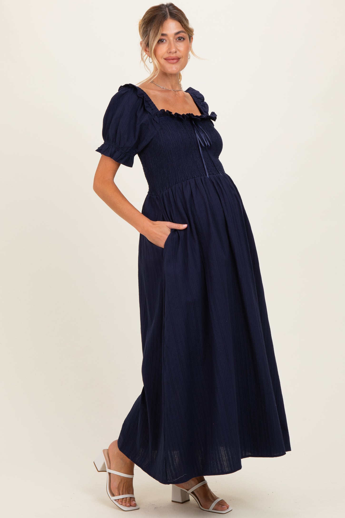 woman wearing a navy blue maternity maxi dress with puff sleeves and pockets, highlighting her baby bump