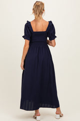 woman wearing a navy blue maternity maxi dress with short ruffled sleeves and a smocked bodice, showing a baby bump