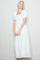 woman wearing a white maxi dress with puffy sleeves and a smocked bodice, smiling against a neutral background