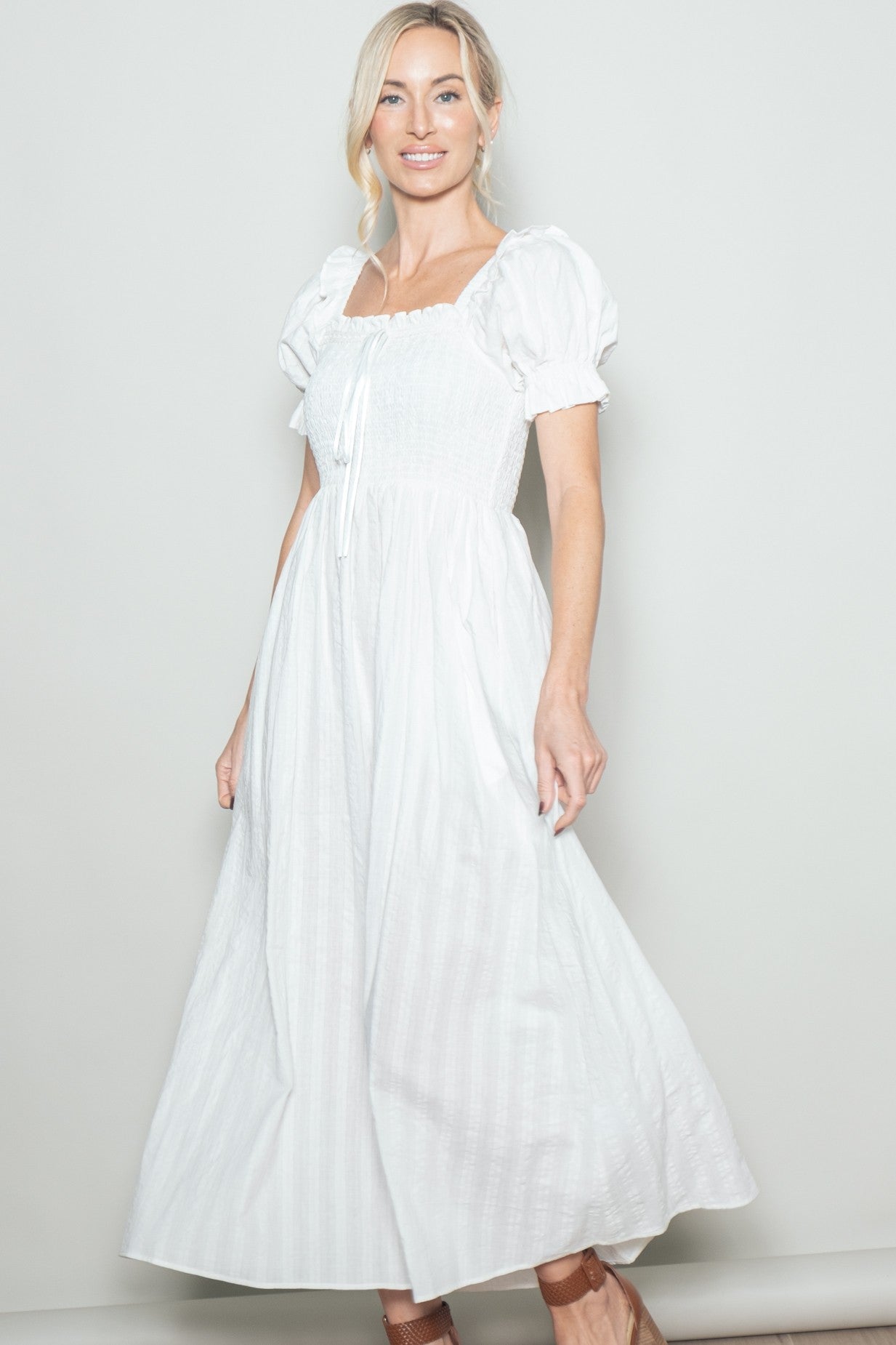 woman wearing a white puff sleeve maxi dress with a smocked bodice and tie detail