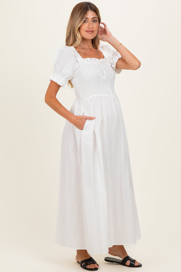 woman wearing a white maternity maxi dress with short puff sleeves and pockets, showcasing her baby bump