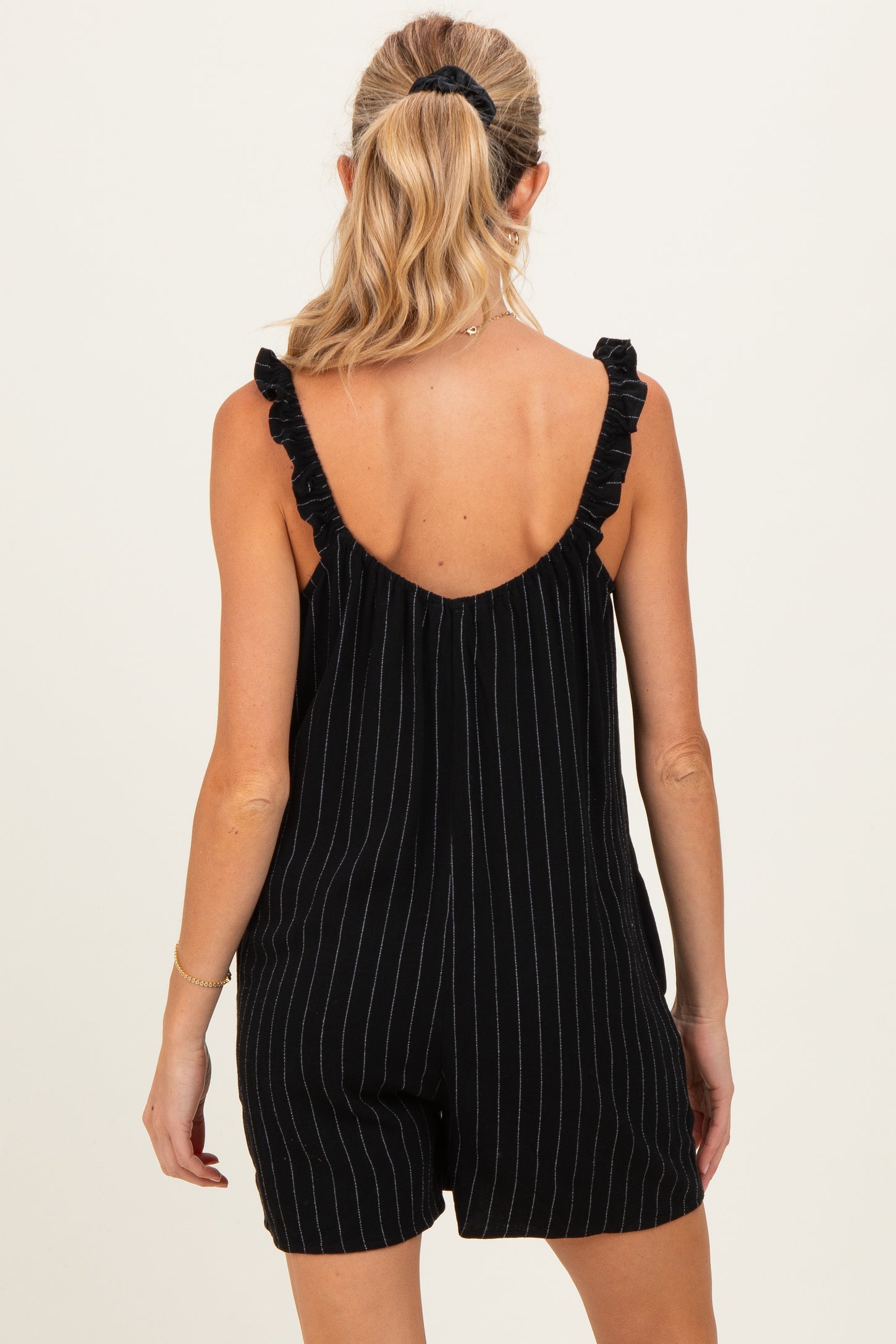 woman wearing a black striped maternity romper with ruffled straps, view from the back