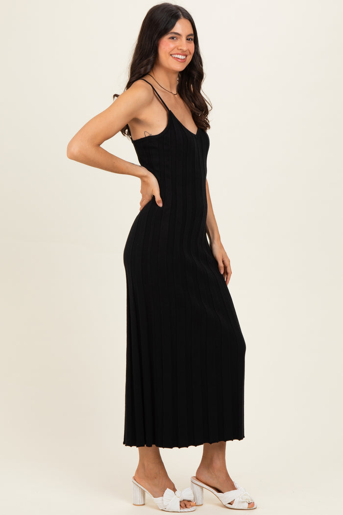 woman wearing a black ribbed maxi dress with thin straps and a fitted silhouette, posing sideways.