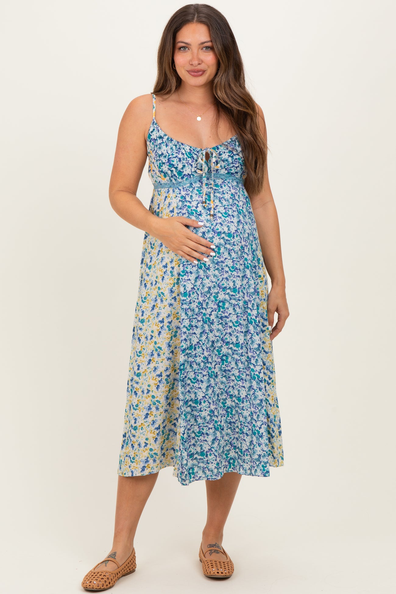 woman wearing a floral midi maternity dress in blue and yellow, holding her baby bump