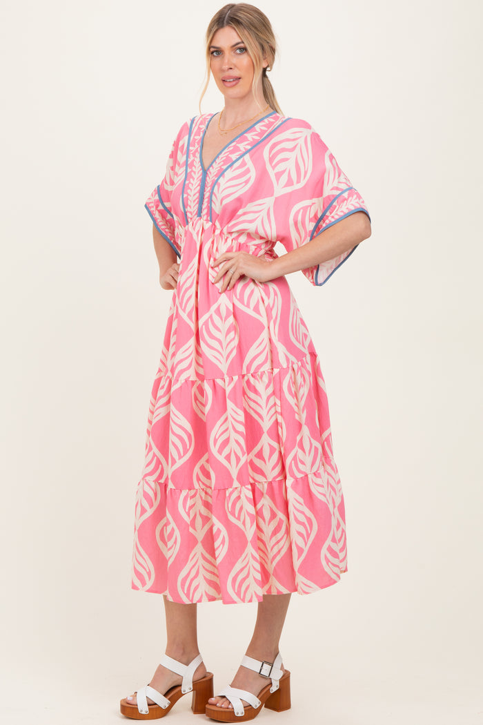 woman wearing a pink boho style dress with leaf patterns and a tiered design, standing with one hand on her hip