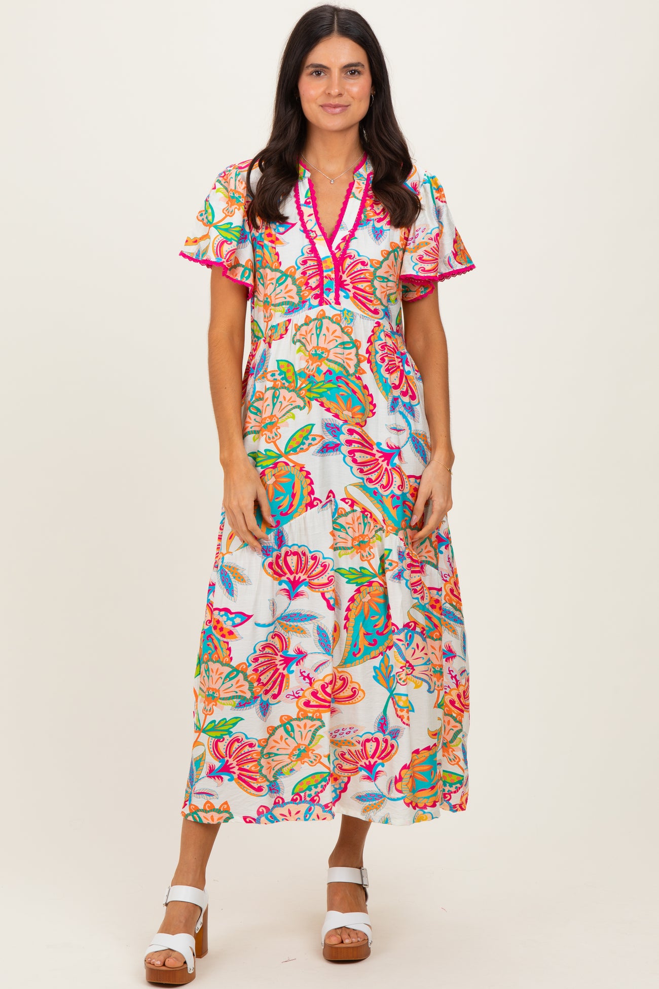 woman wearing a vibrant floral maxi dress with short, ruffled sleeves and a pink trim detail