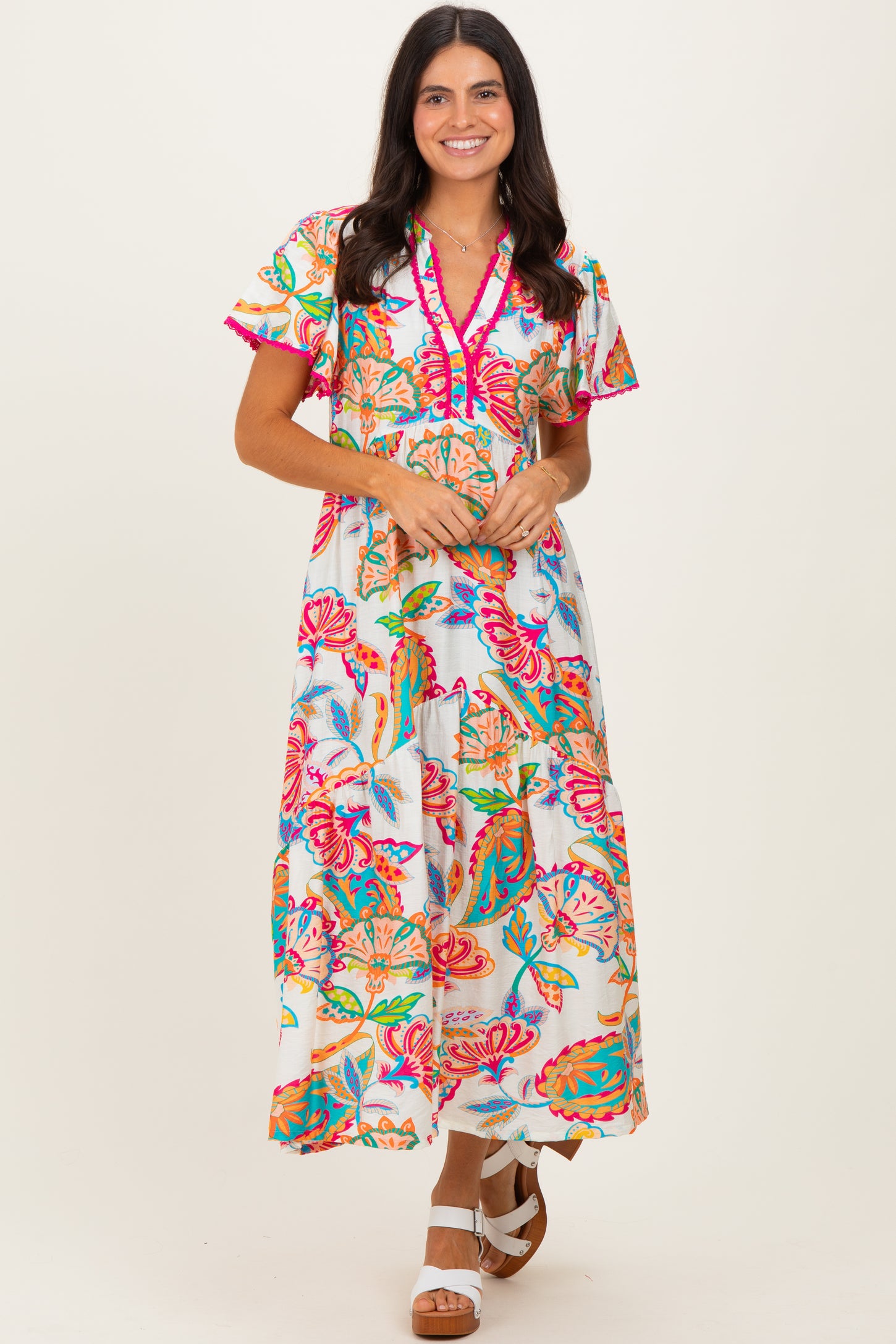 woman wearing a colorful floral maxi dress with short sleeves and a v-neckline, standing against a light background