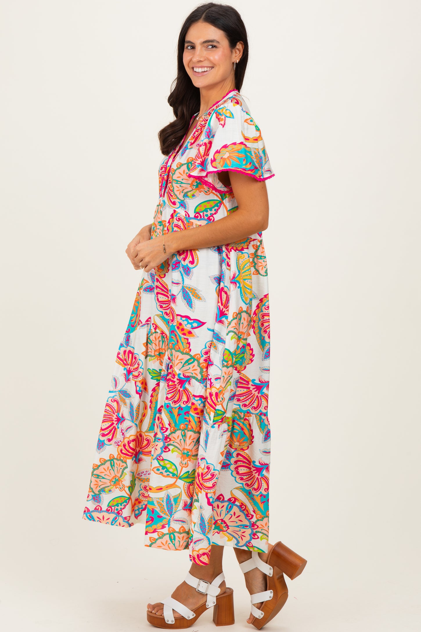 woman wearing a colorful floral maxi dress with ruffled sleeves and tiered skirt, standing sideways