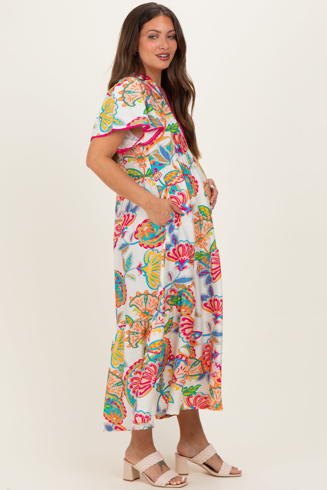 woman wearing a colorful floral maternity maxi dress with short sleeves and pockets, showcasing her baby bump