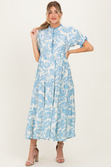 woman wearing a light blue floral printed maternity dress with puff sleeves and a tiered skirt, showcasing her baby bump