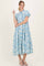 woman wearing a blue floral midi dress with puff sleeves and a high neckline, standing against a neutral background