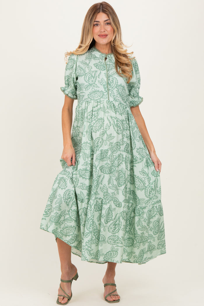 woman wearing a green floral maternity dress with short puff sleeves and a tiered skirt, highlighting her baby bump
