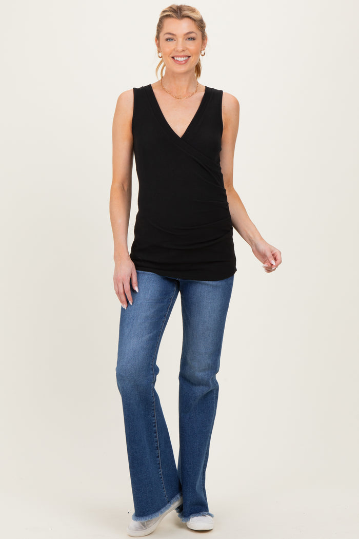 woman wearing a black sleeveless maternity top with a v-neck and ruched side, paired with blue flared jeans