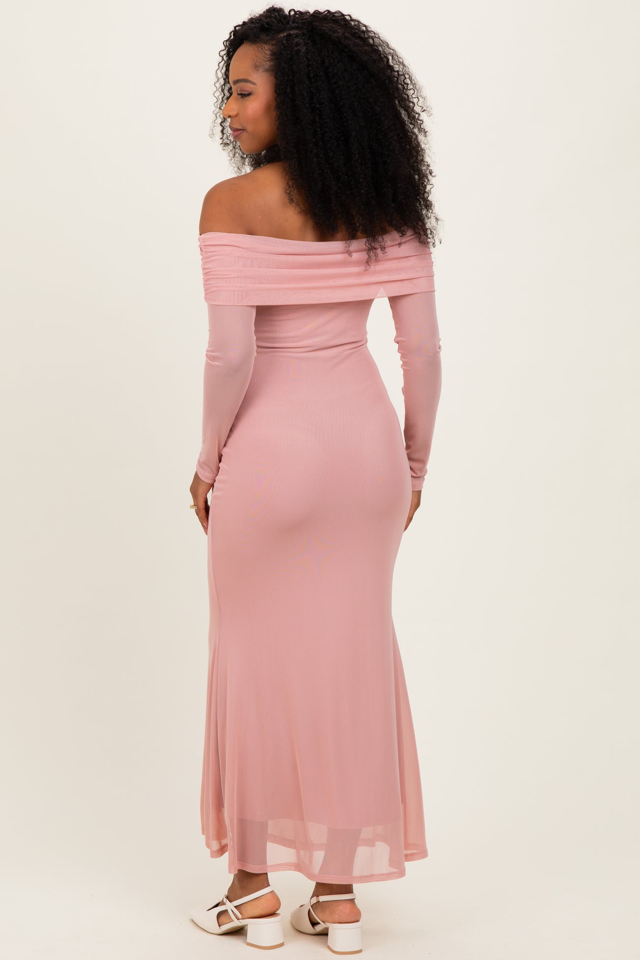 woman wearing a light pink off-the-shoulder maxi dress with long sleeves and a fitted silhouette