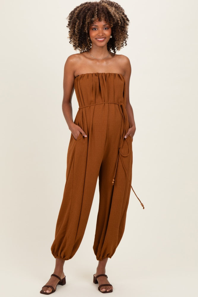 woman wearing a brown strapless maternity jumpsuit with pockets and a drawstring waist