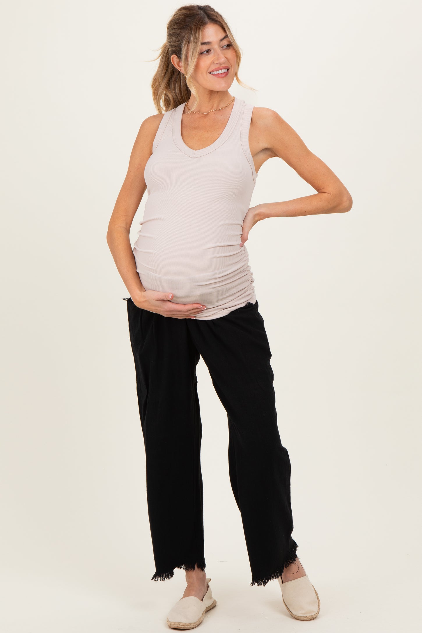 woman wearing a light beige maternity tank top and black maternity pants, showing off her baby bump